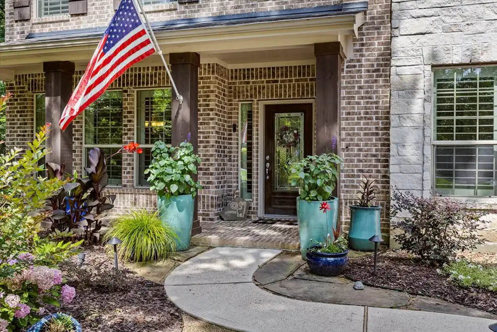 front porch of two story brick home with american flag and landcaping