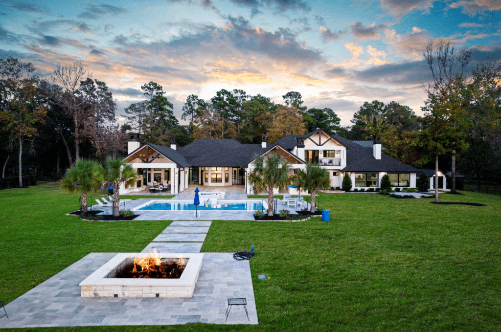 Back yard of a home for sale in Conroe, TX showing covered patio, large back yard, custom fire pit, and in-ground pool.