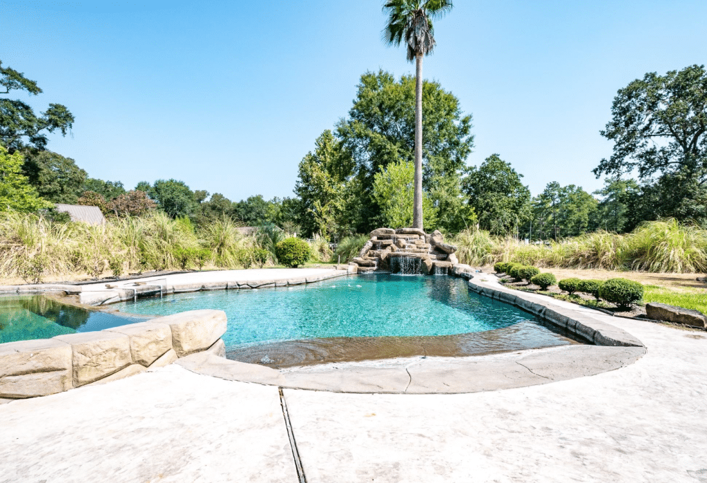 Back yard of a home for sale in Conroe, TX with in-ground pool and hot tub.