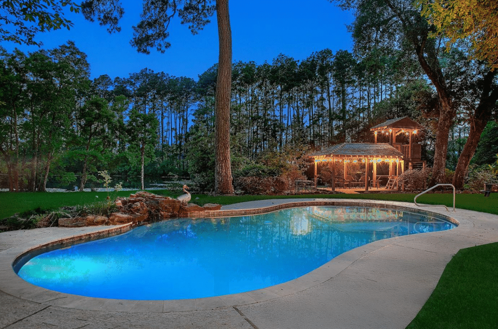 Back yard of a home for sale in Conroe, TX showing in-ground pool, large lot, and covered sitting area.