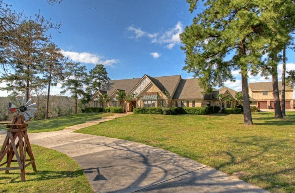 Exterior of a home for sale in Conroe, TX showing front lawn with mature trees and decorative wind mill.